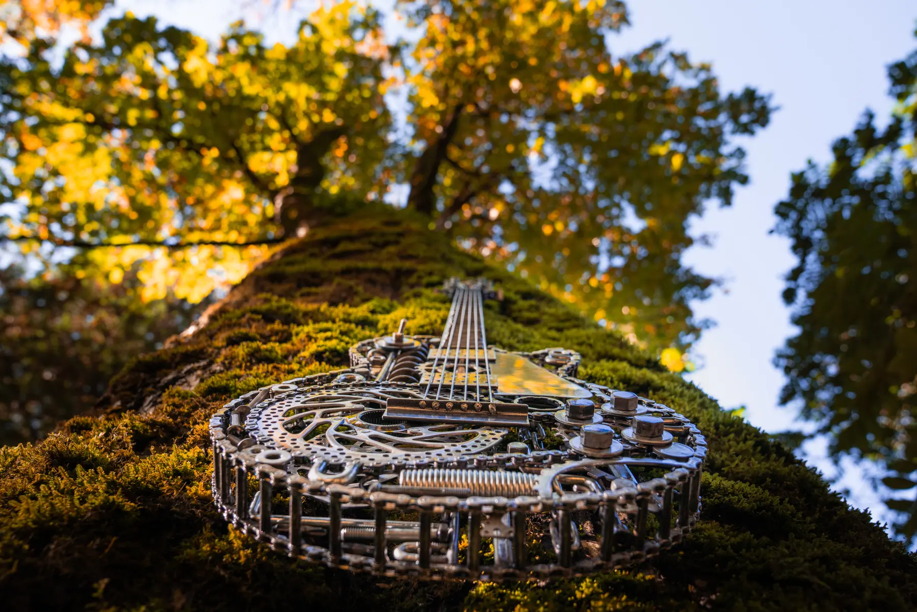 Grace, a Les Paul–style guitar welded from bicycle parts, hanging on a mossy tree in golden light